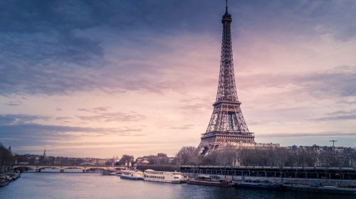 A beautiful wide shot of Eiffel Tower in Paris surrounded by water with ships under the colorful sky